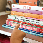Toddler hand pointing at stack of children's books | Representation in Children's Books